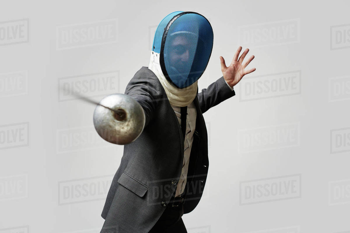 Businessman in fencing mask and formal suit attacking his rival with foil to defense himself and his business or company in economically hard period Royalty-free stock photo