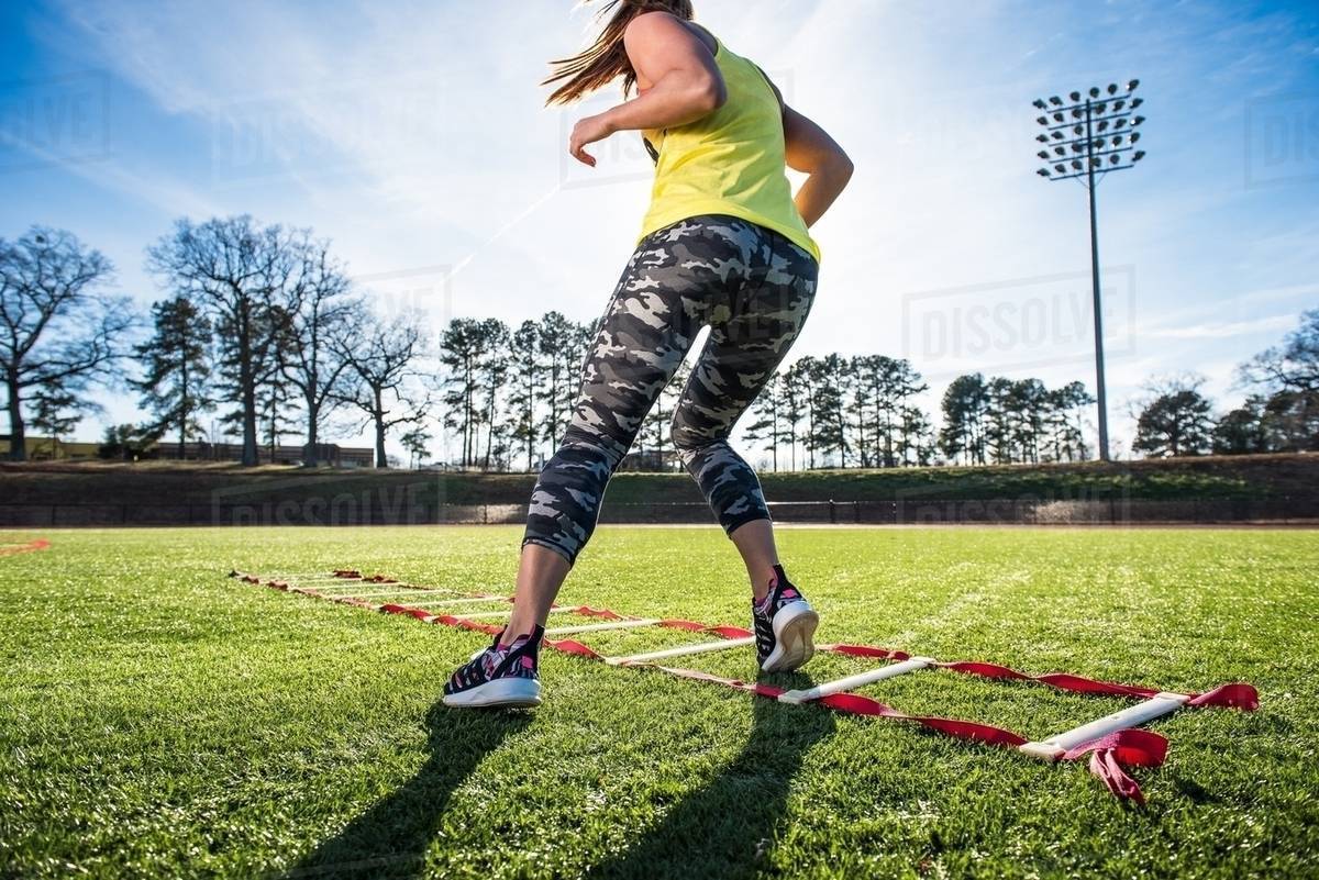 Female athlete training with agility ladder on sports field Stock