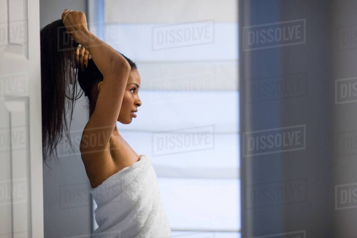 Young woman wrapped in white towel tying up long black hair in bathroom Royalty-free stock photo