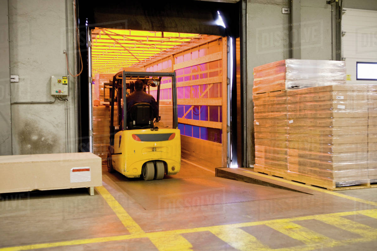 Forklift operator loading wrapped pallets of cardboard boxes onto