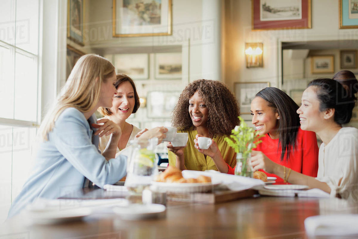Smiling women drinking coffee and talking at restaurant table Stock