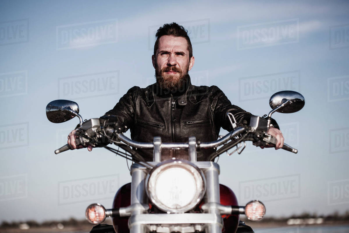 Portrait of confident biker sitting on motorcycle against sky Royalty-free stock photo